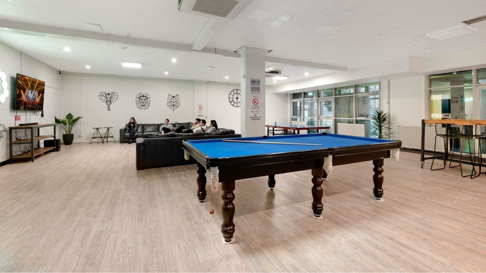 People sitting on couches and playing pool in a room at La Trobe University – Menzies College.