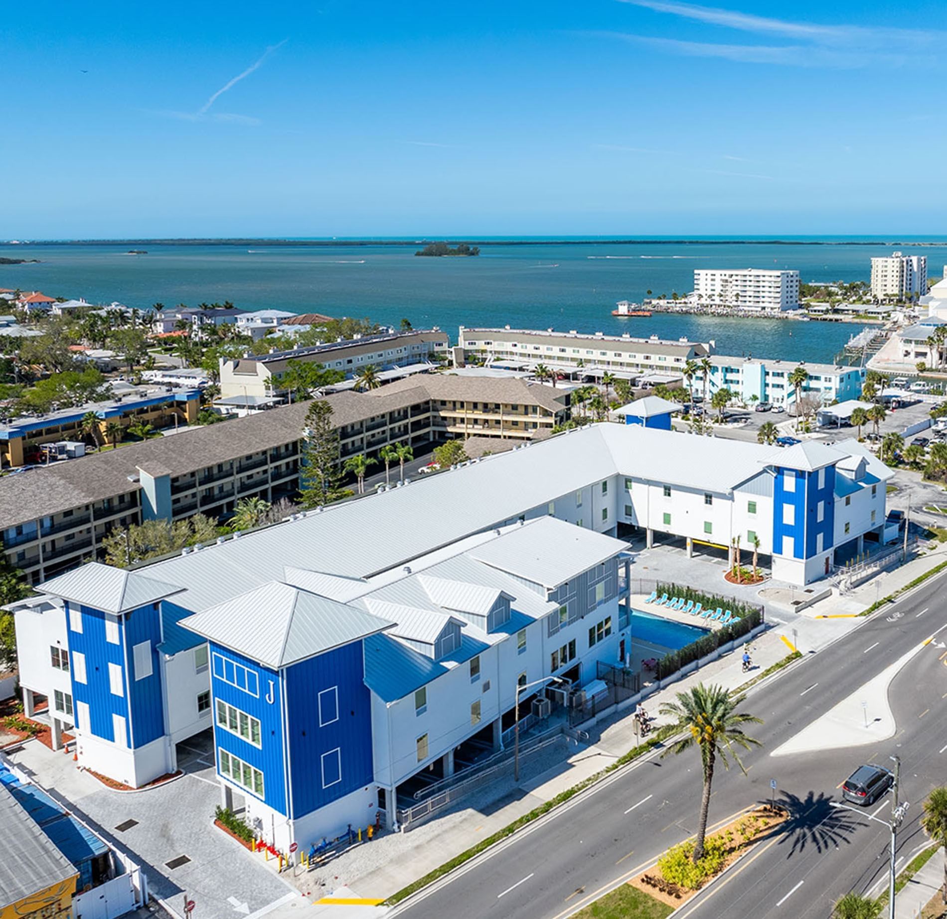 Aerial view of a multi-story hotel with blue accents and a white roof, featuring a pool and parking lot.