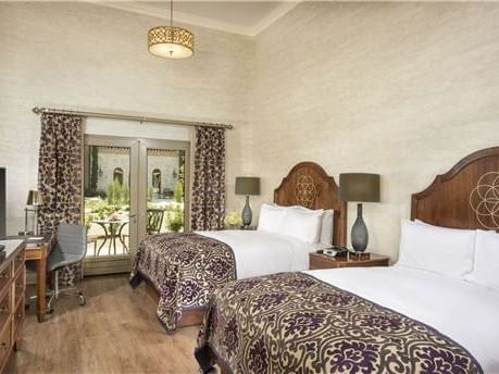 A room which includes Two queen size beds, a writing desk and  glass double doors leading out to the patio.