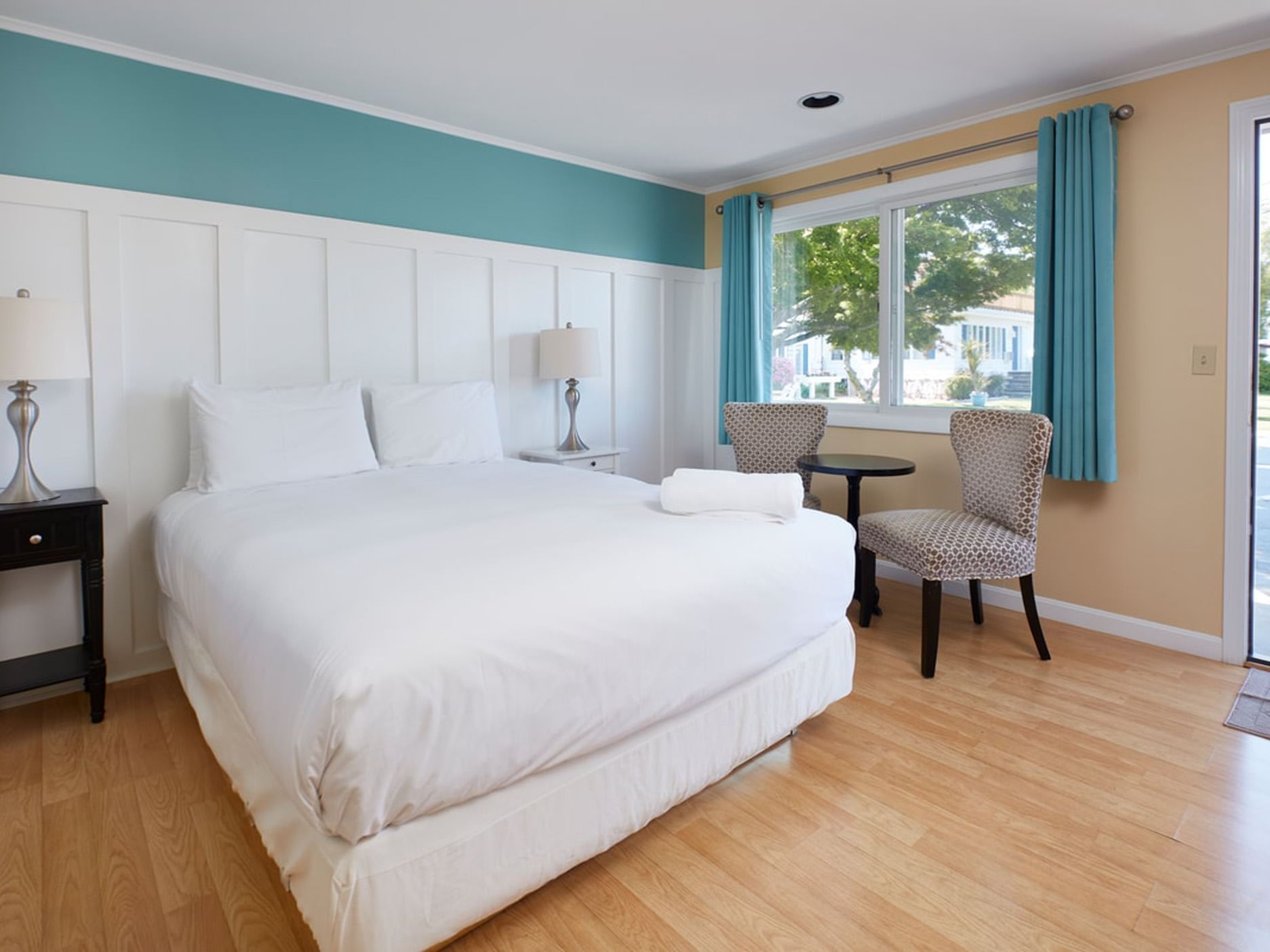 Bed with table lamp by the window and seating in One Queen at Breezeway Boutique Hotel