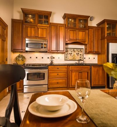 A dining table set with plates and glasses in a kitchen with wooden cabinets and a stovetop at The Stanley Hotel