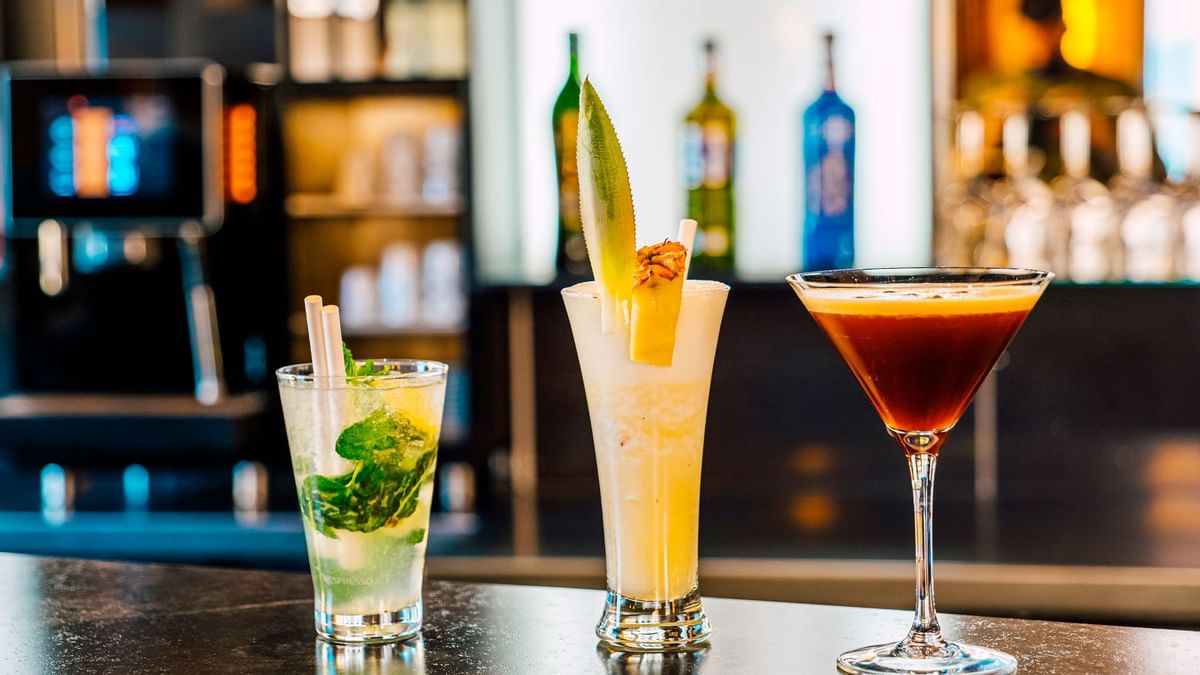 Trois cocktails différents avec des décorations uniques présentés sur un comptoir de bar.