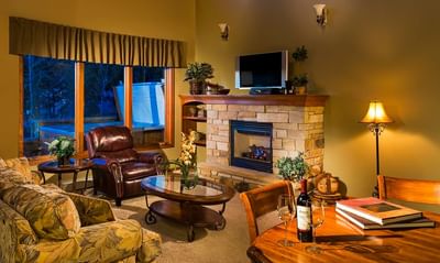 A warm living area with a stone fireplace, a TV, and a leather armchair with a view of a hot tub at The Stanley Hotel