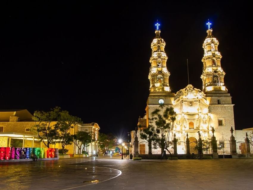 Catedral iluminada con torres gemelas por la noche en una plaza de la ciudad cerca de Camino Real Hotels