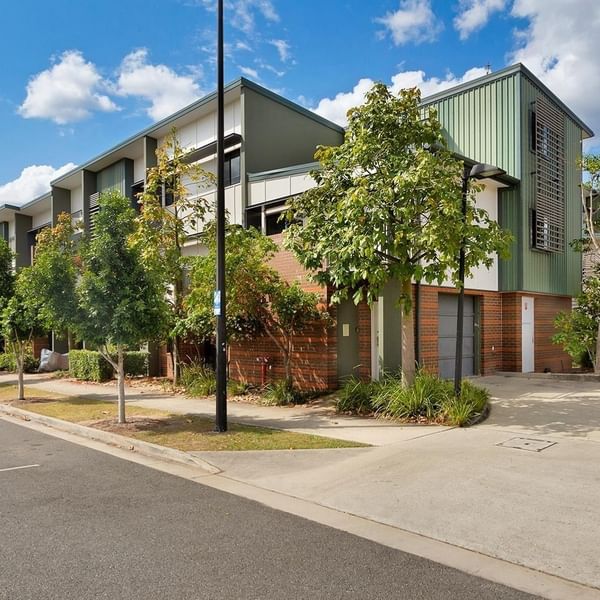 Modern multi-story student accommodation building with green and brick facade surrounded by young trees and landscaping.