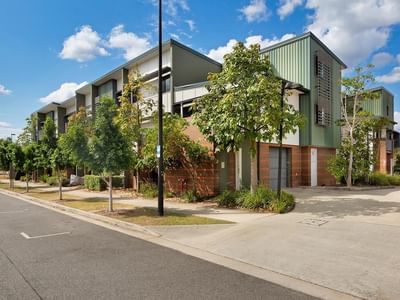 Modern multi-story student accommodation building with green and brick facade surrounded by young trees and landscaping.