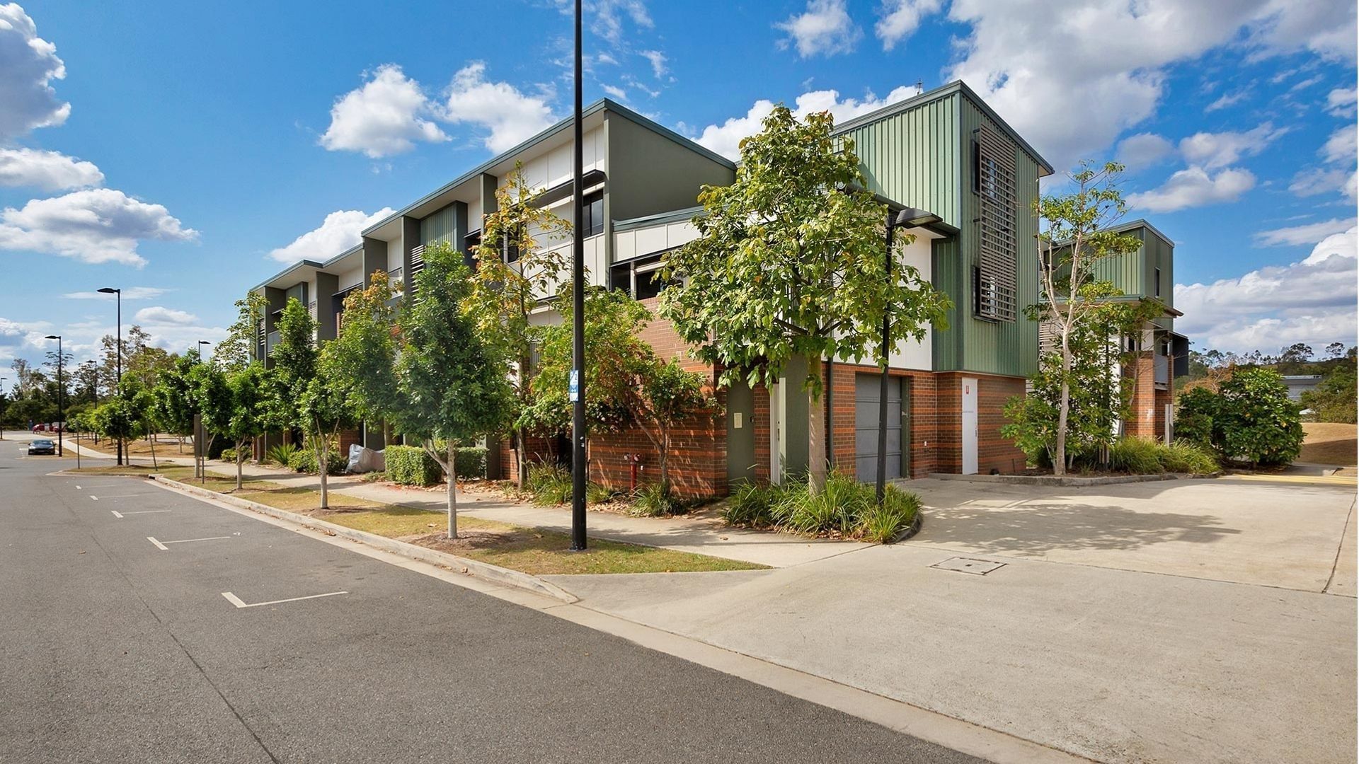 Modern multi-story student accommodation building with green and brick facade surrounded by young trees and landscaping.