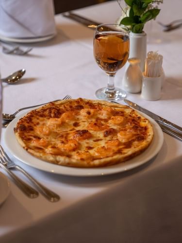 Freshly prepared pizza served on a white plate on Al Firdous Restaurant table setting at Saja Warwick Madinah
