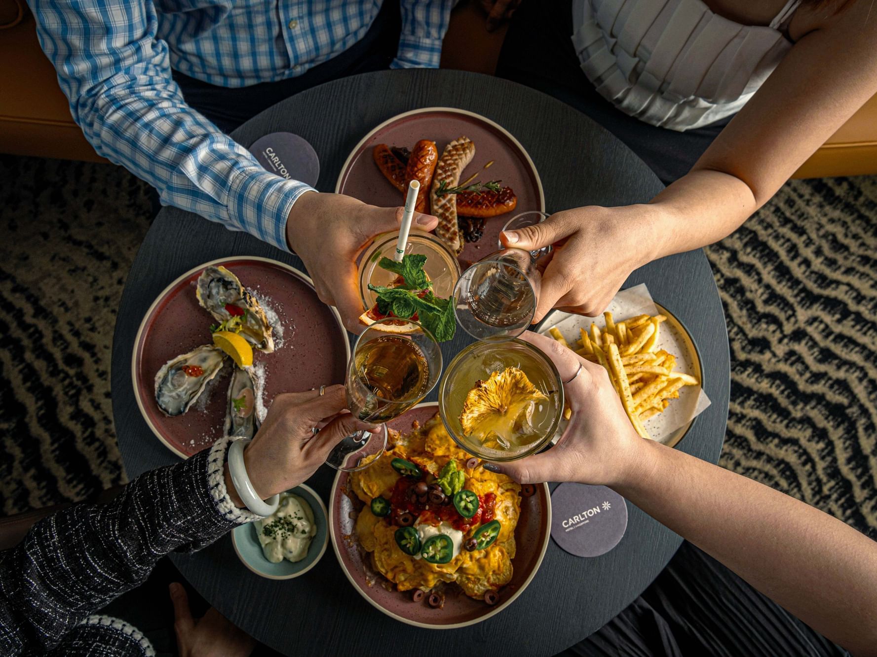 Four people toasting cocktails at dining table in Carlton Hotels Singapore