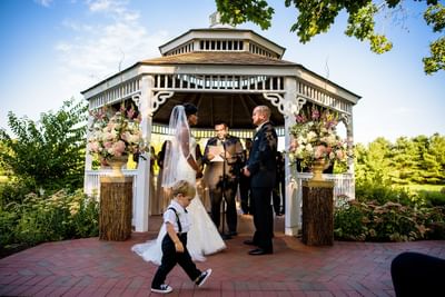 Outdoor wedding ceremony in white gazebo with floral arrangements at Aramark Chauncey Conference Center