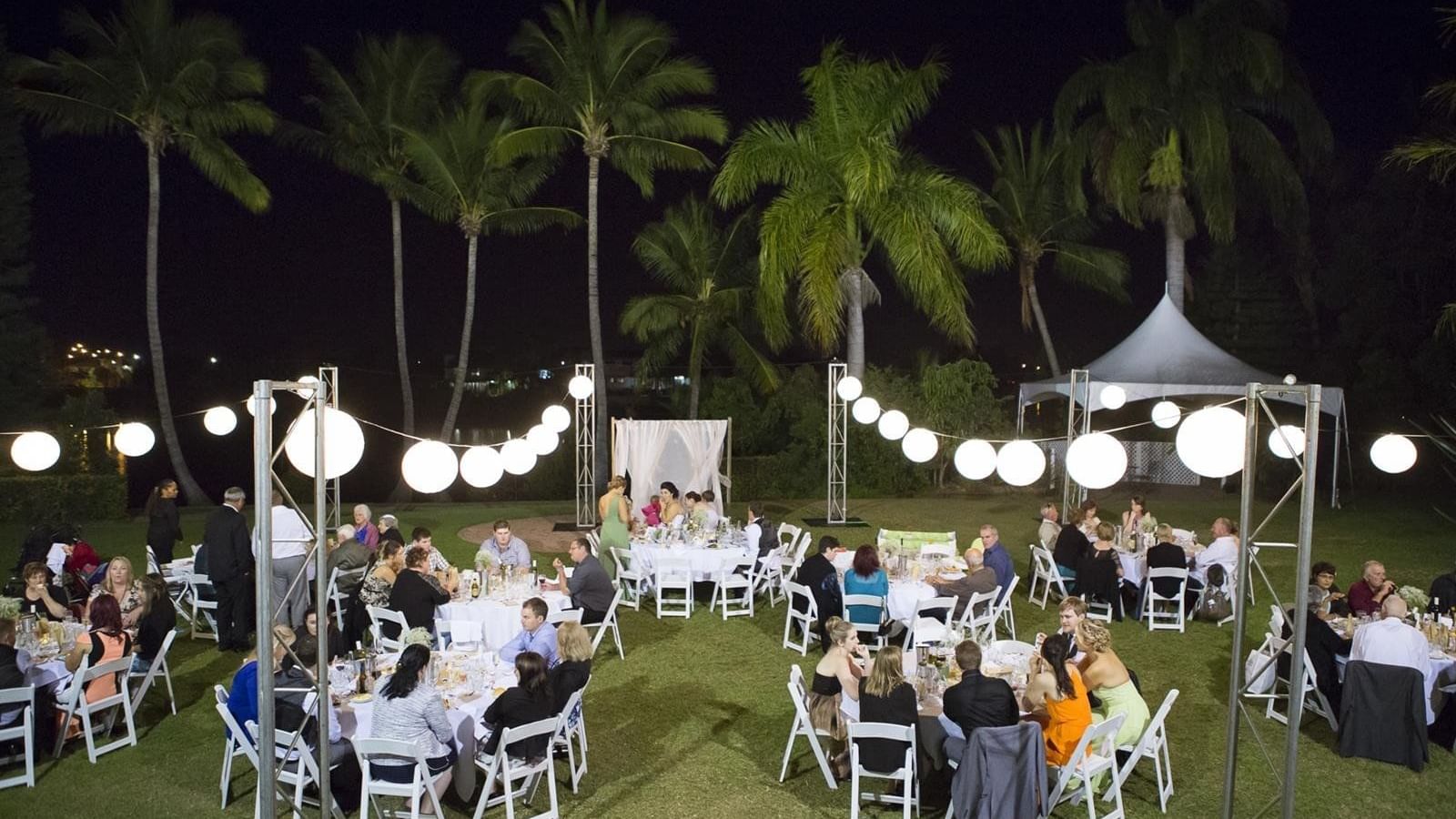 Guests at well-lit outdoor venue with round tables and hanging lanterns in Mercure Hotel Townsville
