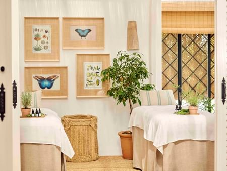 Bright event space with botanical artwork, woven furnishings, and white-draped tables near latticed windows.