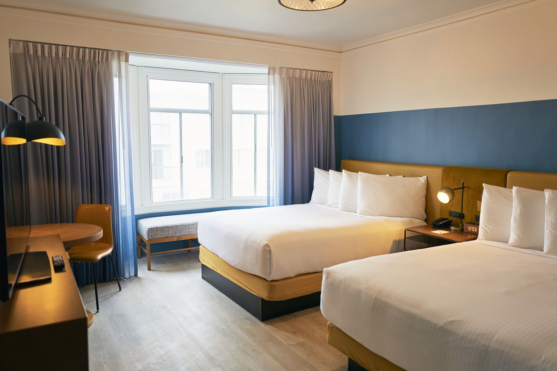 A hotel room with two queen beds, a desk, and a window.