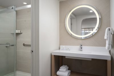 Premium Mini Suite Two Queens with a circular mirror, white sink, and glass shower at The Harrison Hotel Downtown Hollywood