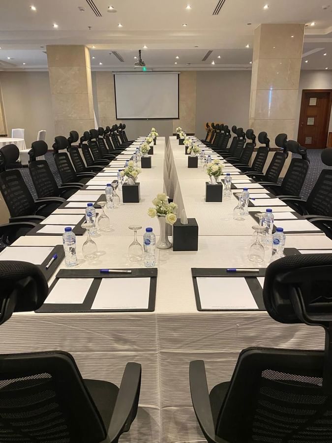 Long conference table with black mesh chairs by white roses in Crystal Meeting Room at Naviti by Warwick Al Khobar
