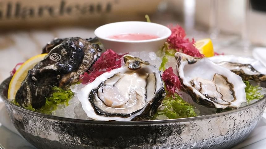 Chilled platter of fresh oysters on ice, garnished with lemon and seaweed in Park Lounge at Park Hyatt Saigon