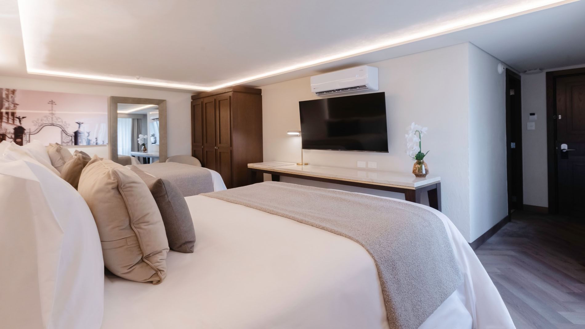 Perspective view of a hotel double room with white bedding and a wall-mounted TV in Queen Deluxe at Quinta Real Puebla
