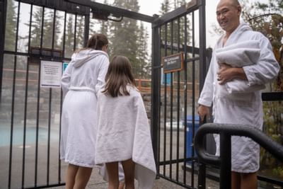 Woman and girl in white robes walking toward gated hot tub entrance at Blackstone Mountain Lodge