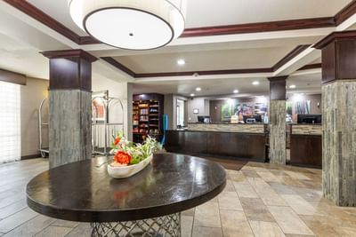 Hotel lobby featuring a circular wood table with flowers in front of the check-in desk at Branson Hillside Hotel