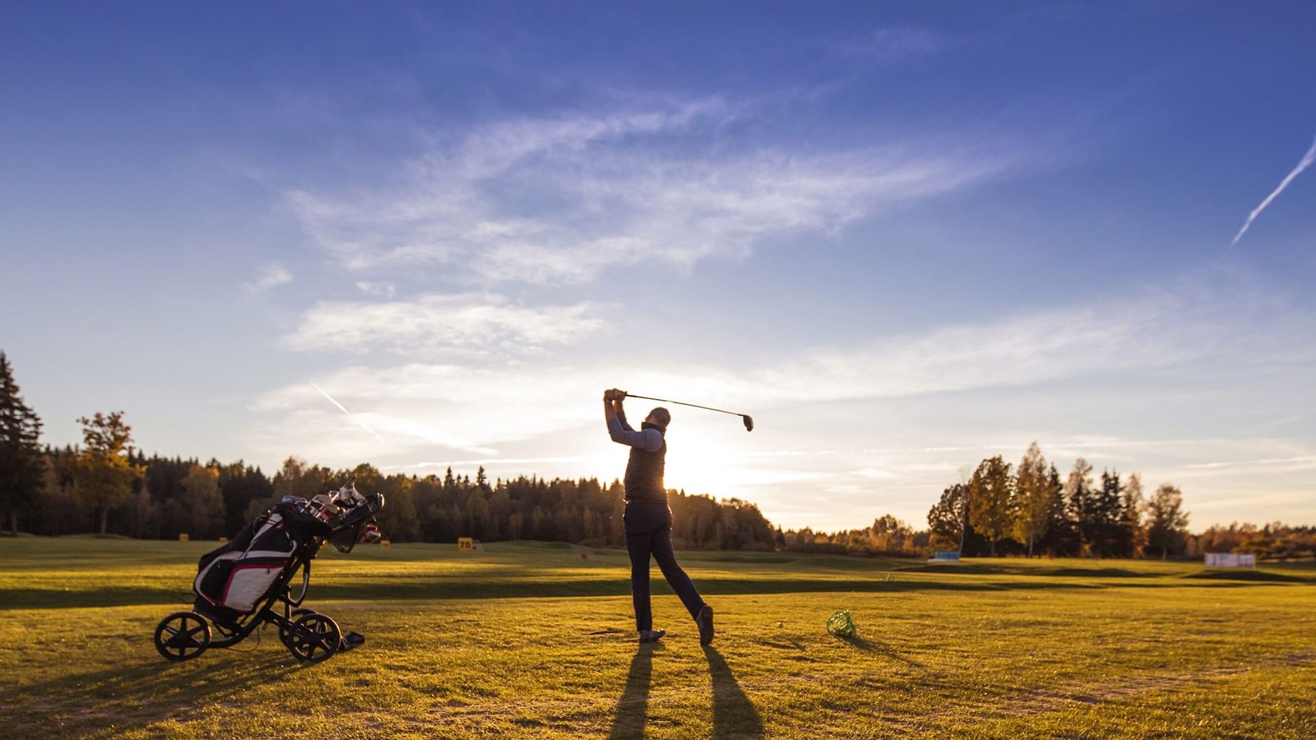 Golfer swinging club on course with golf cart nearby at Falkensteiner Hotel & Spa Jesolo