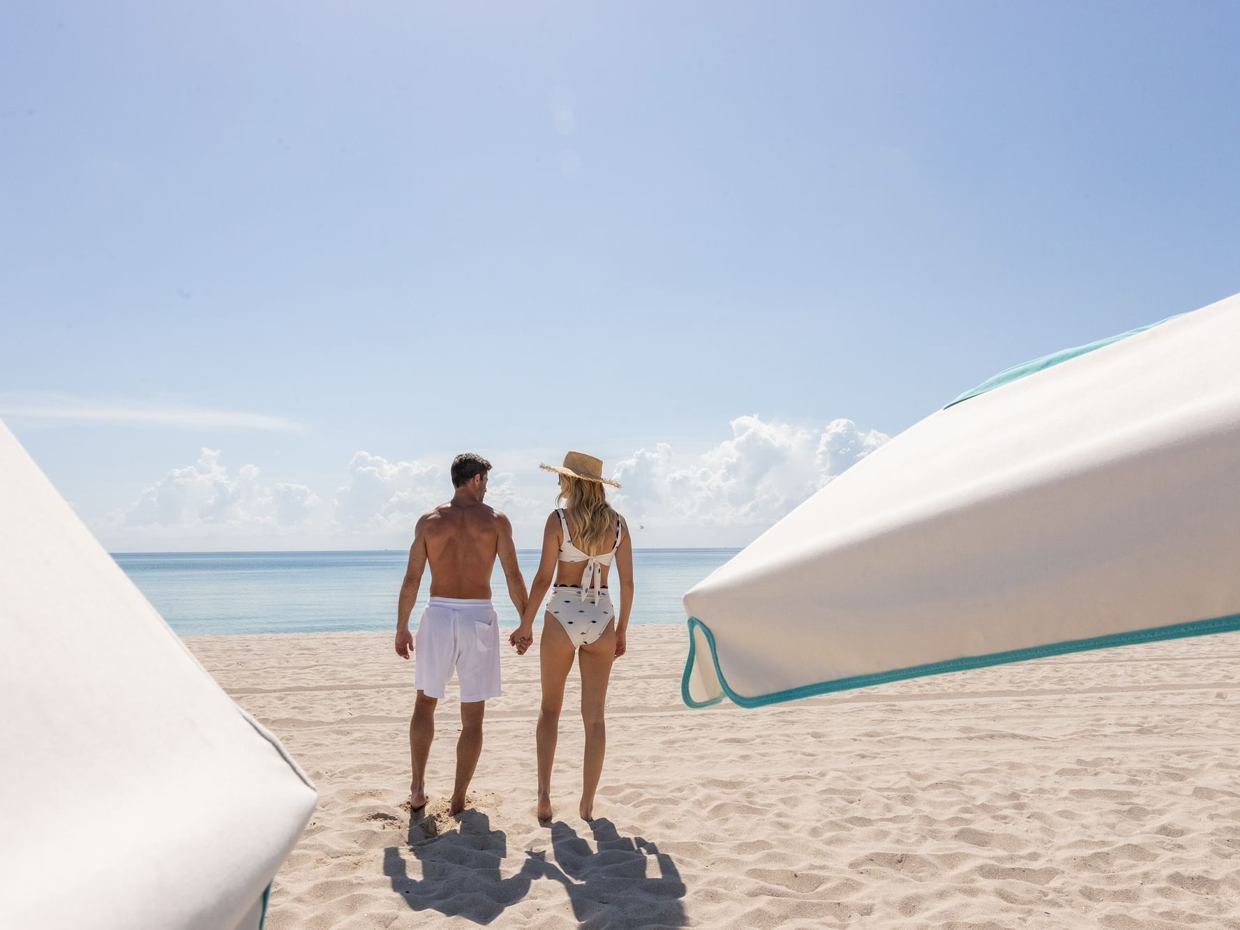 Couple holding hands and walking on a sunny beach at The Savoy Hotel & Beach Club