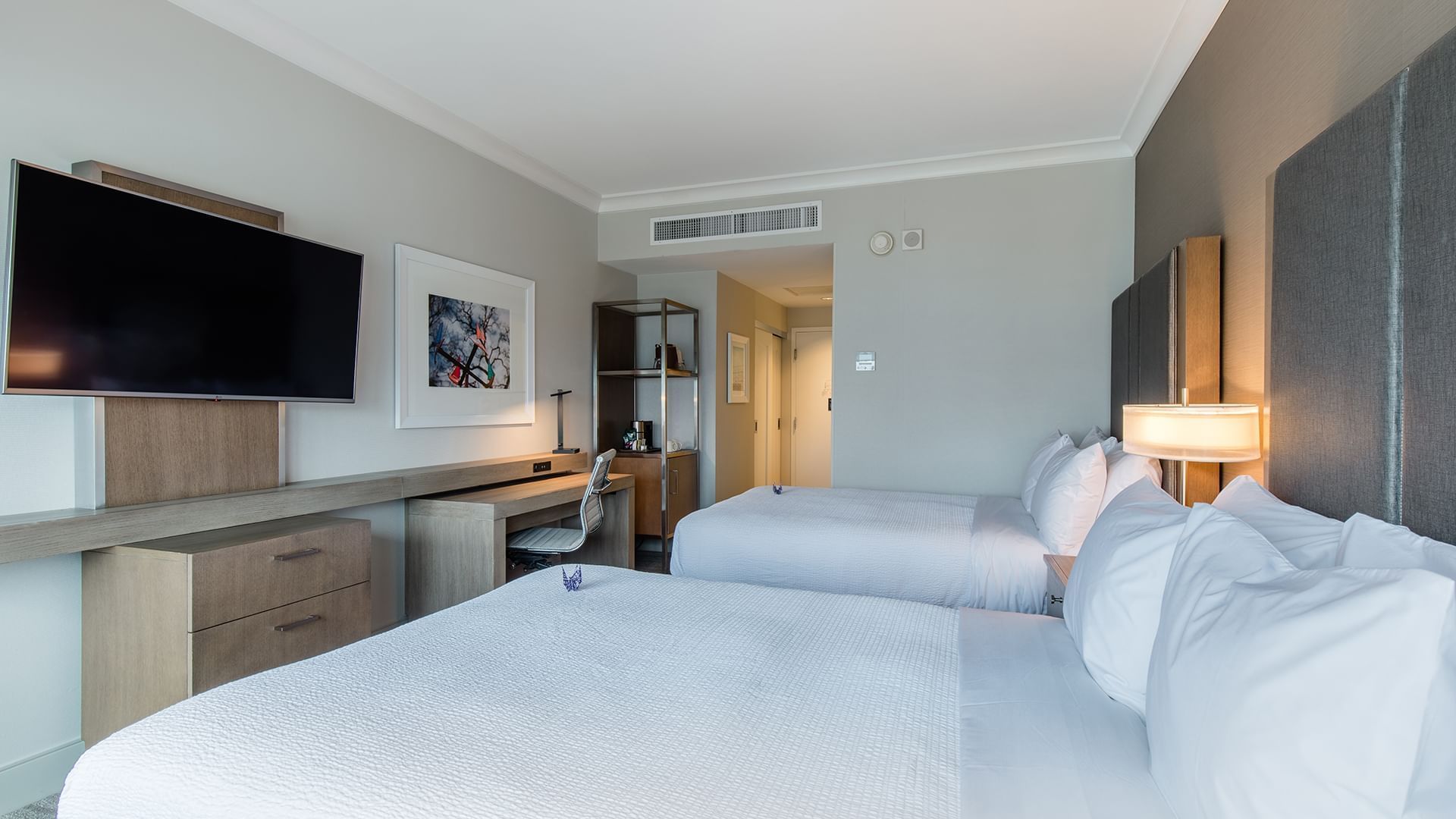 A hotel room with two double beds, a desk, and a TV on the wall.