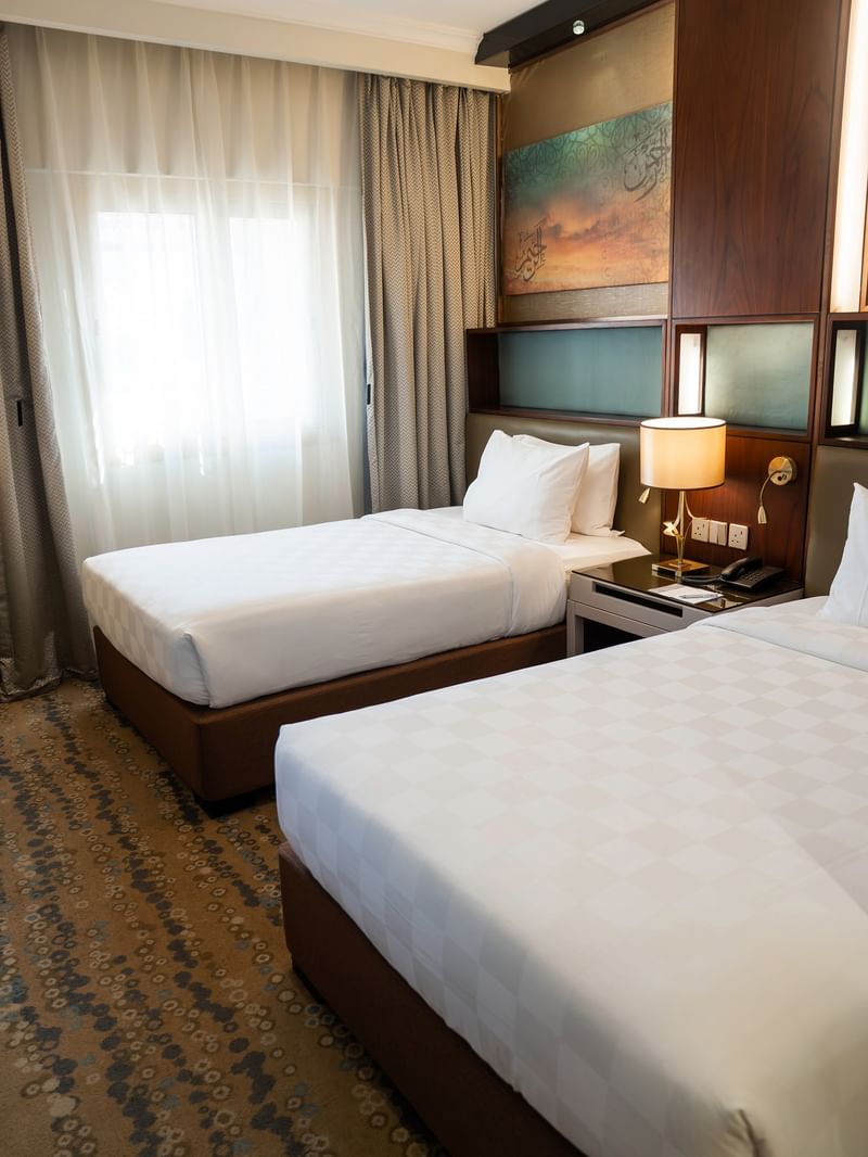 سريران أبيضان مع وسائد وطاولة جانبية في غرفة مزدوجة قياسية في فندق سجى ورويك المدينة المنورة.