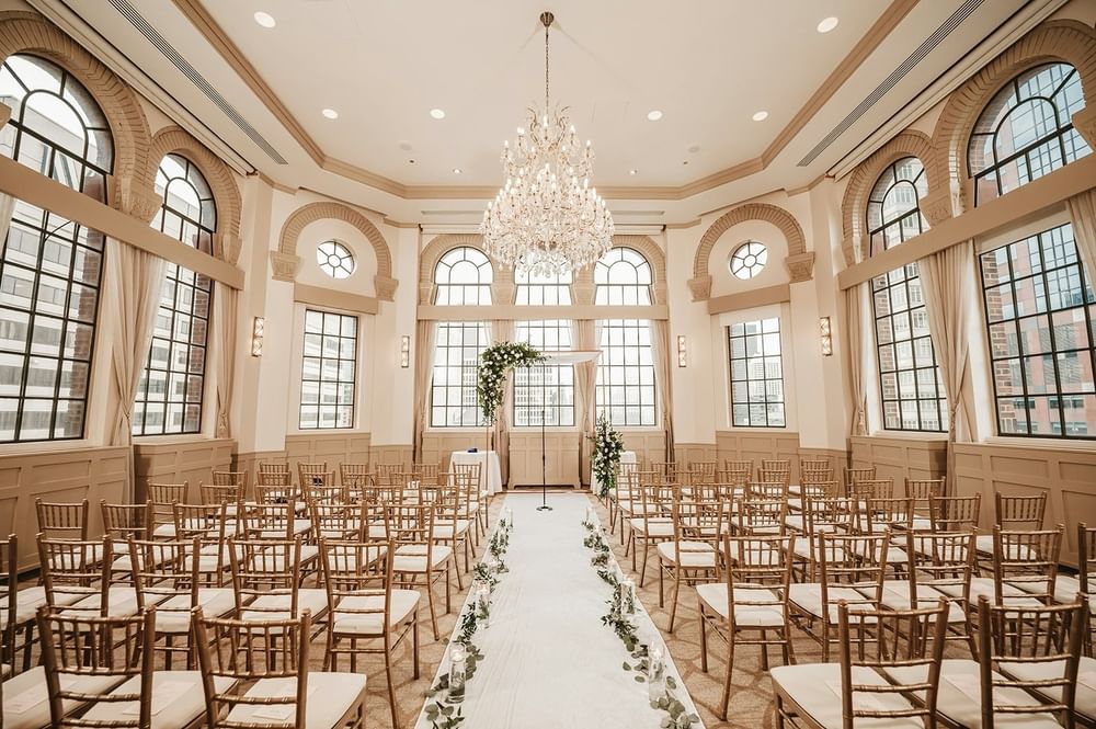 Ceremony space with rows of chairs and a flower-adorned aisle under a grand chandelier at Warwick Allerton Chicago