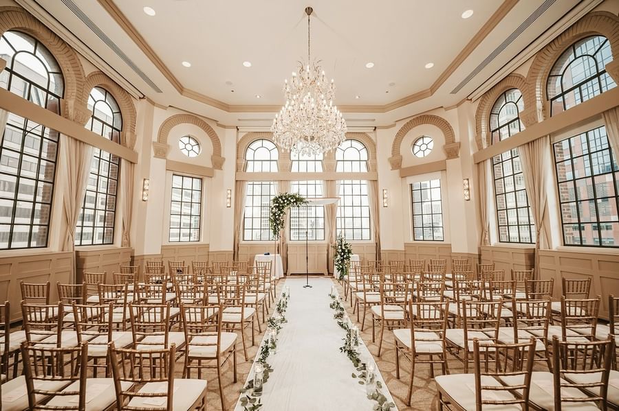 Ceremony space with rows of chairs and a flower-adorned aisle under a grand chandelier at Warwick Allerton Chicago