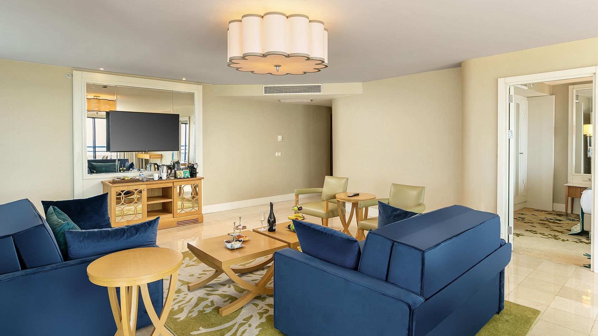 Titanic Deluxe Lara–Colonel Suite’te mavi kanepeli, ahşap mobilyalı ve avizeli lüks salon.