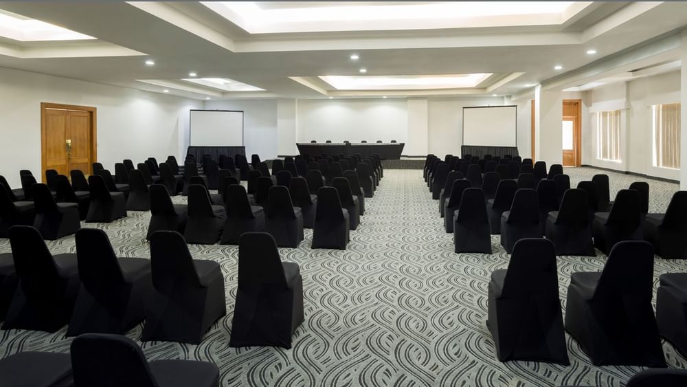 Black chairs in rows by a projector screen under a tray ceiling in the Bangkok at Real Inn Mexicali