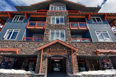Low-angle view of Blackstone Mountain Lodge featuring a stone facade, large windows, and wooden accents