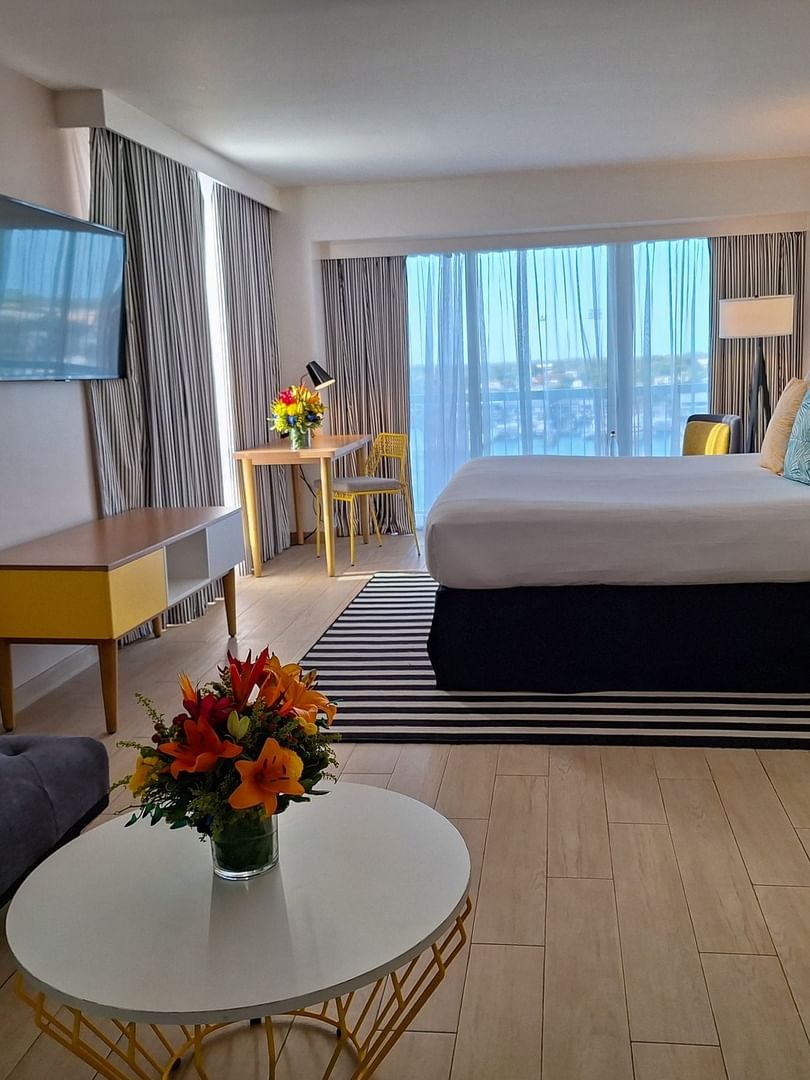 Harbour Premium Balcony with a dark sofa by a round table and a king bed at Warwick Paradise Island Bahamas