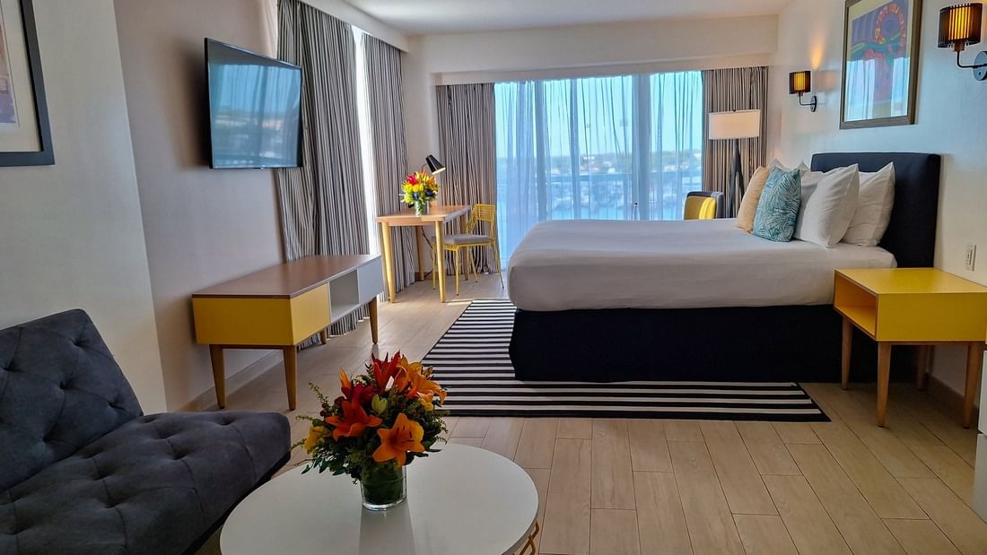 Harbour Premium Balcony with a dark sofa by a round table and a king bed at Warwick Paradise Island Bahamas