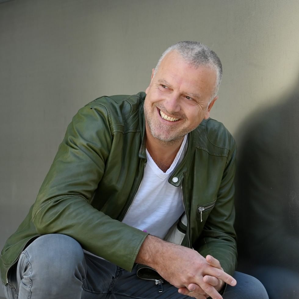 Smiling man in green leather jacket seated for Crime Festival Reading featuring Bernhard Aichner's Totenfrau Die Rückkehr