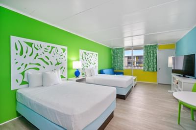 Upper Floor Poolview Efficiency room with two beds, green walls sofa & large window with colorful curtains at Kokomo Suites