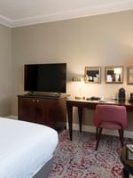 Pink chair by a wooden desk under gold mirrors near a TV and a king bed in Superior Room at Warwick Paris Champs Elysées