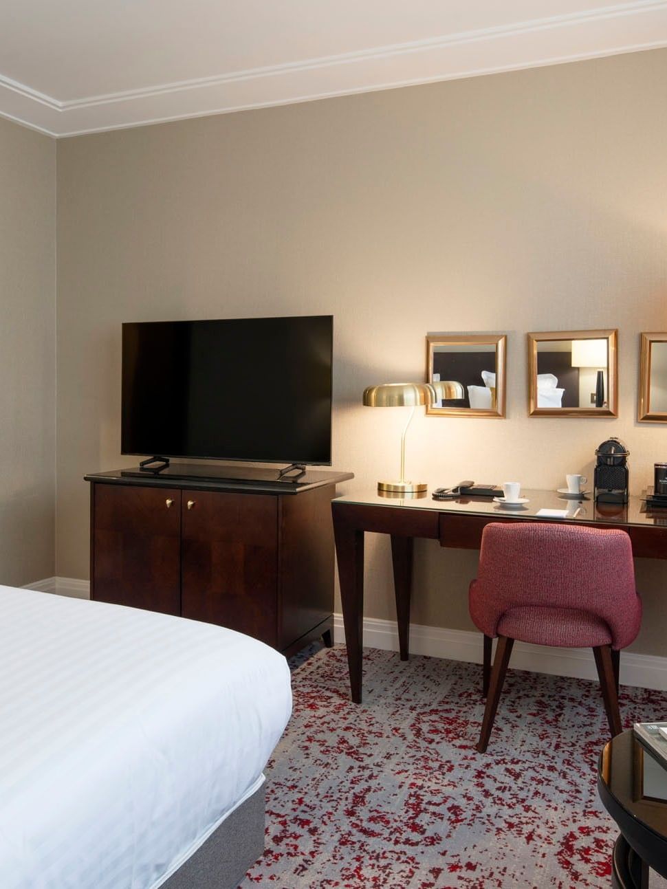 Pink chair by a wooden desk under gold mirrors near a TV and a king bed in Superior Room at Warwick Paris Champs Elysées