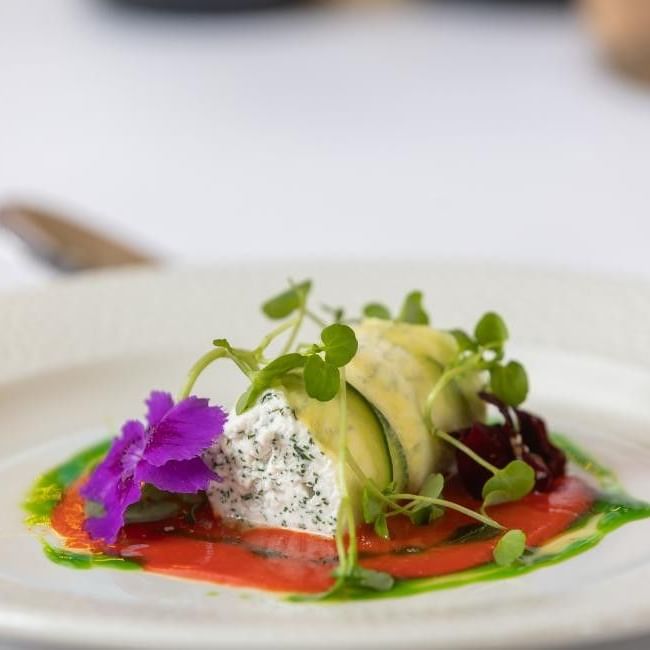 Elegantly plated starter with smoked salmon, soft cheese, avocado ribbons, microgreens and edible purple flower.