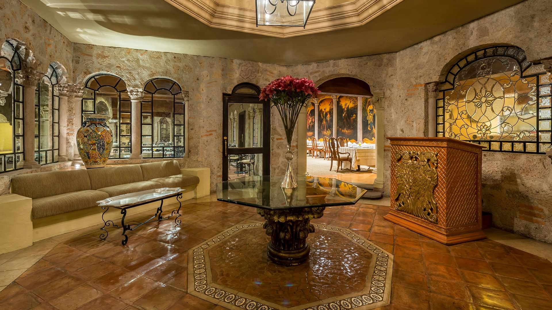 Elegante vestíbulo con arcos de cantera, mesa central con flores y vista al comedor en Quinta Real Aguascalientes