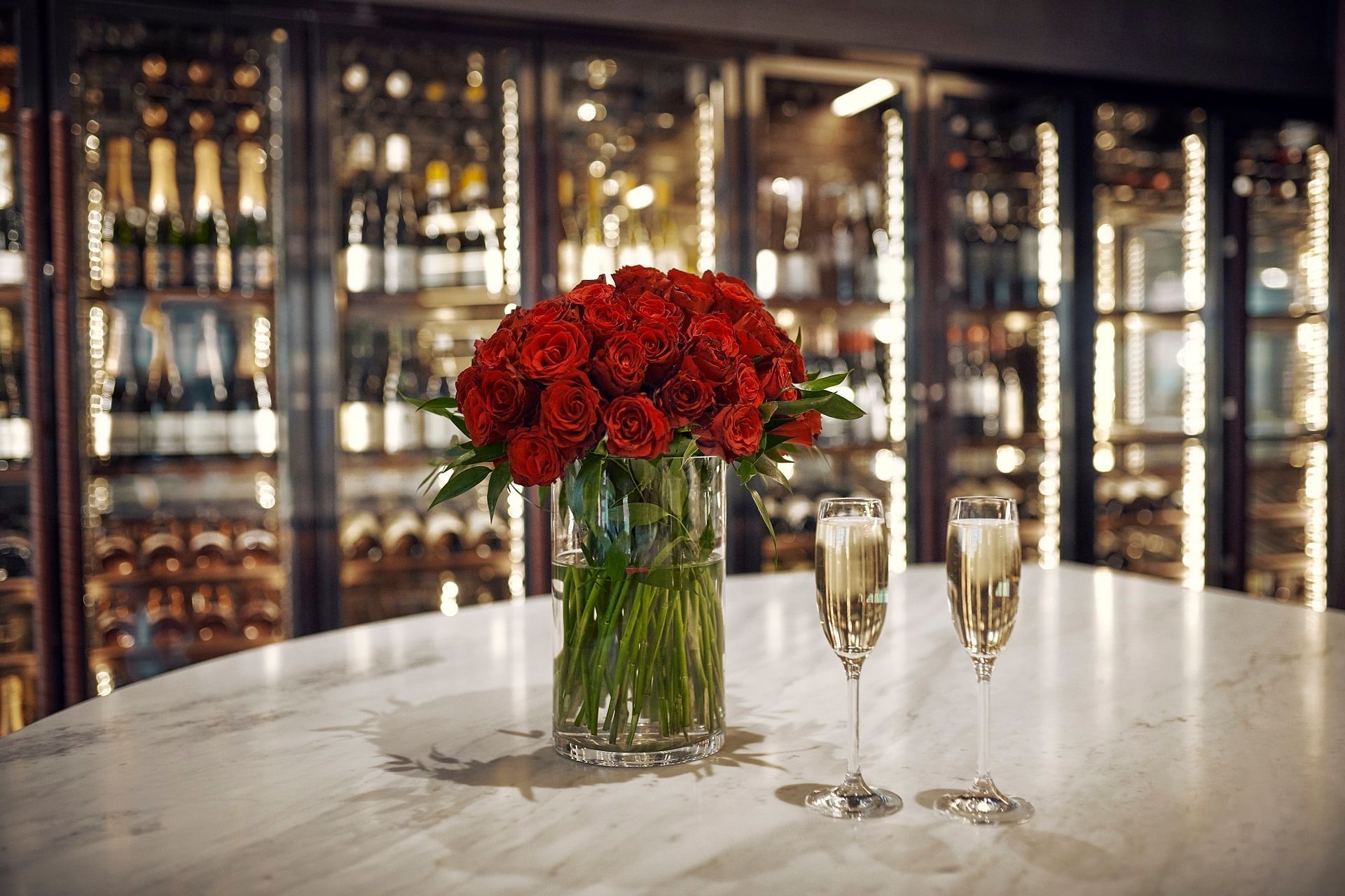 En bukett rosor som står på en vit marmorskiva. Bredvid står två glas med champagne.