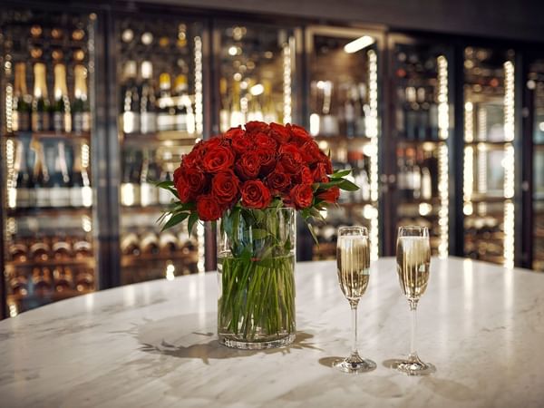 Red roses in a vase and two glasses of champagne on a table in a luxurious restaurant.