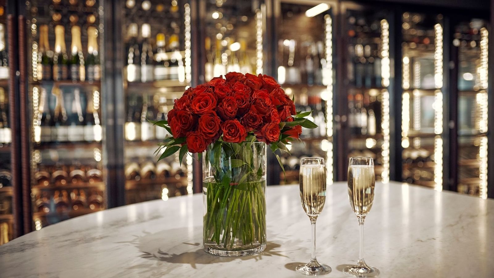 Red roses in a vase and two glasses of champagne on a table in a luxurious restaurant.