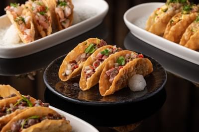 Tacos filled with meat, topped with cilantro and onions beside shrimp tacos on a dark surface at The Kitchens