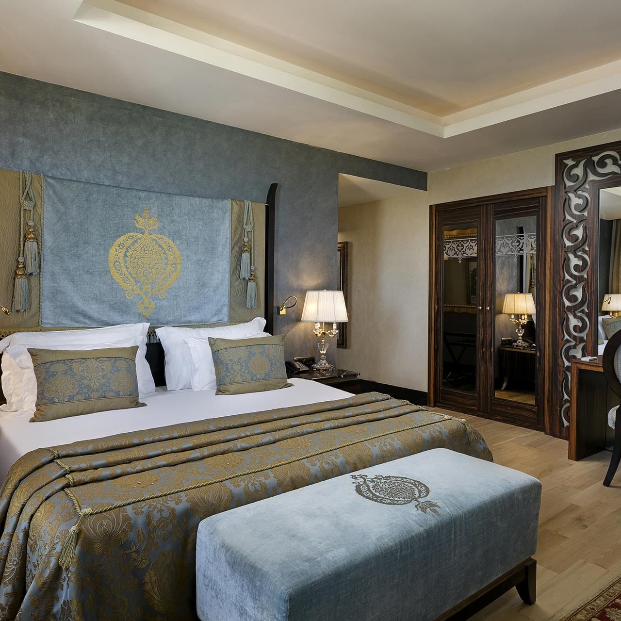 Элегантная спальня в королевском двухуровневом люксе отеля Titanic Mardan Palace с большой кроватью, прикроватными тумбами, лампами, декоративным изголовьем, зеркальной дверью и стильной зоной отдыха
