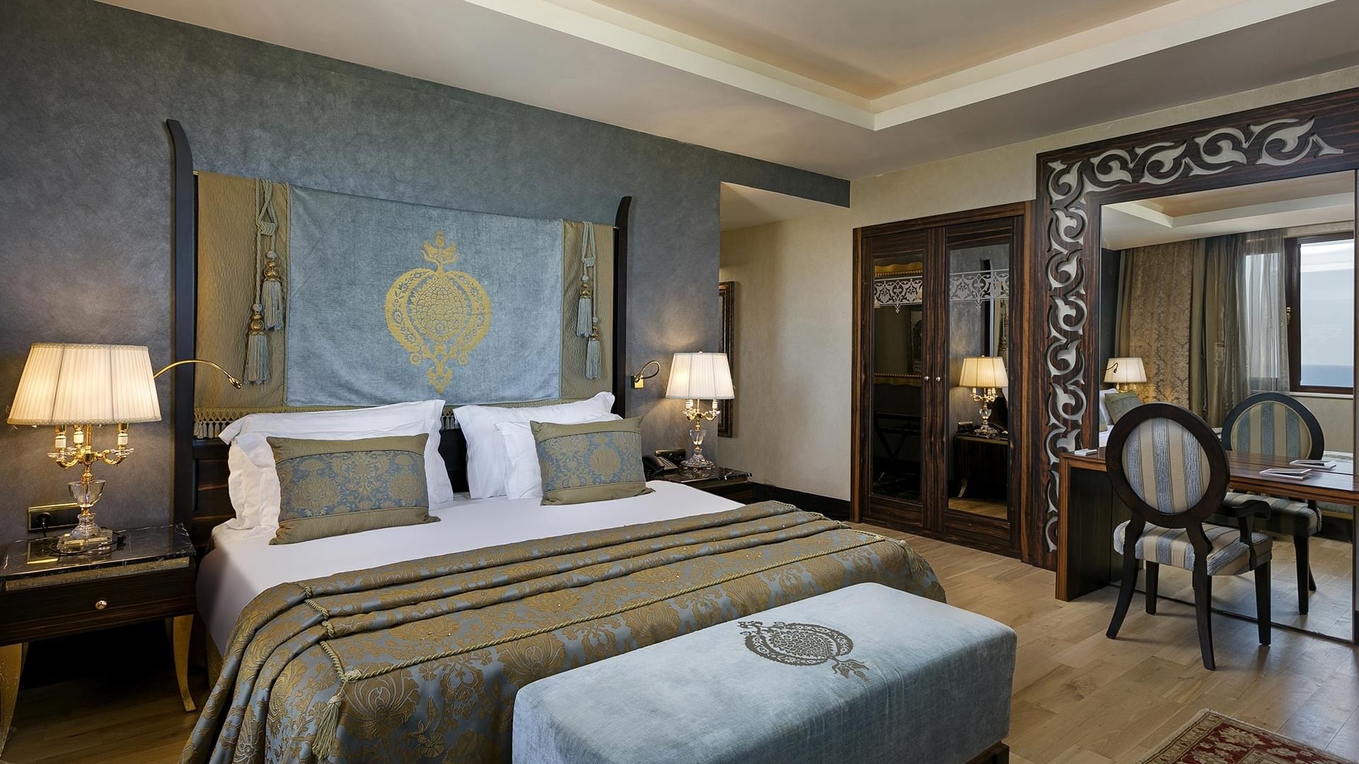 Элегантная спальня в королевском двухуровневом люксе отеля Titanic Mardan Palace с большой кроватью, прикроватными тумбами, лампами, декоративным изголовьем, зеркальной дверью и стильной зоной отдыха