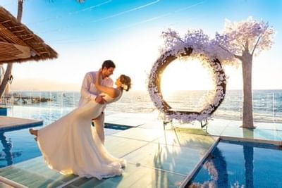 Bride and groom embracing by poolside with ocean view and floral arch at Playa Los Arcos Puerto Vallarta 2023