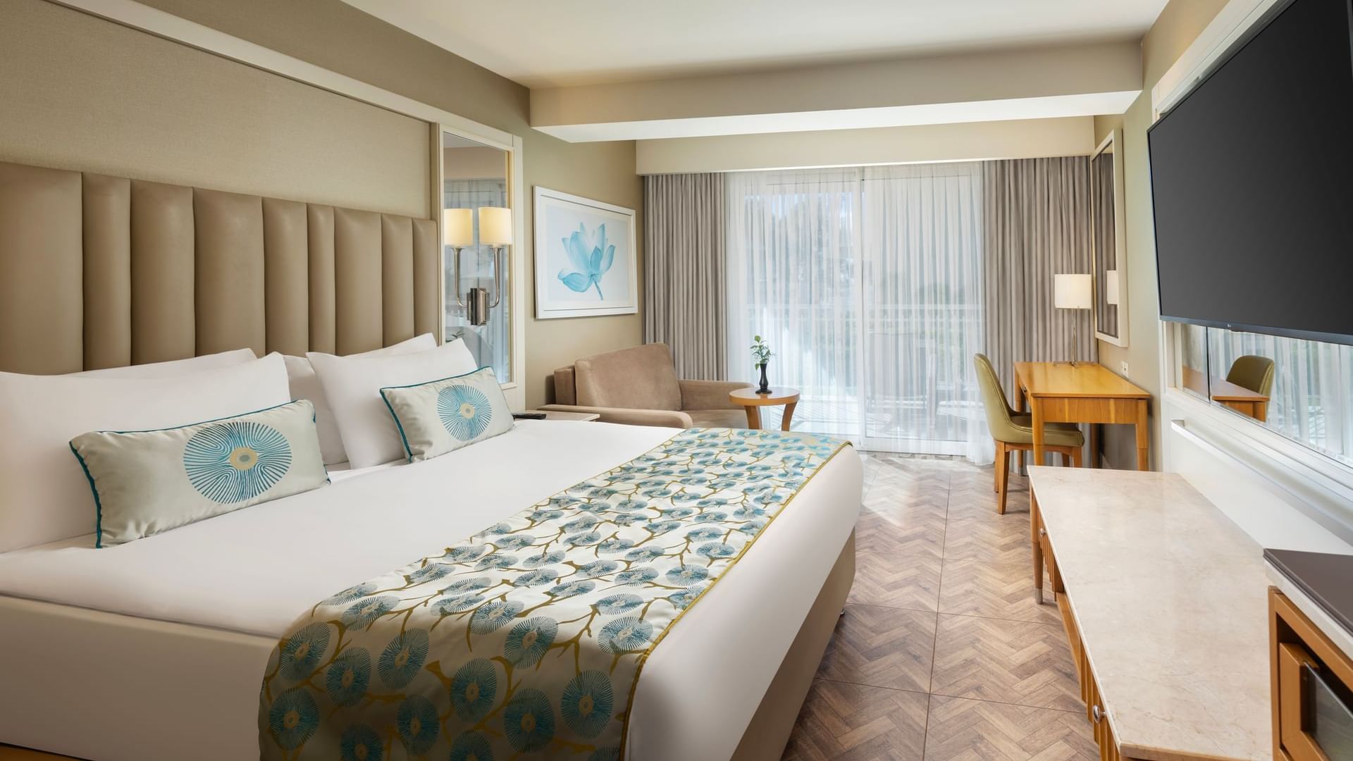 Titanic Deluxe Lara – Annex Standard Pool’da geniş yataklı, koltuklu ve büyük televizyonlu zarif bir oda.