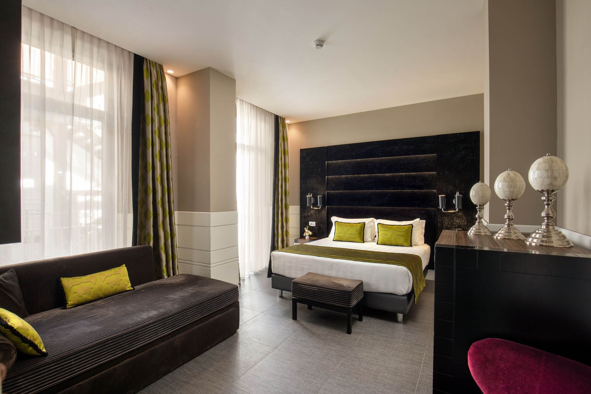 Bed with an ottoman by the window and seating in Family Room at The Glam Hotel