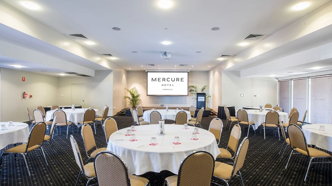 Crystal Room with cabaret setup, beige chairs, and a large screen at Mercure Hotel Townsville